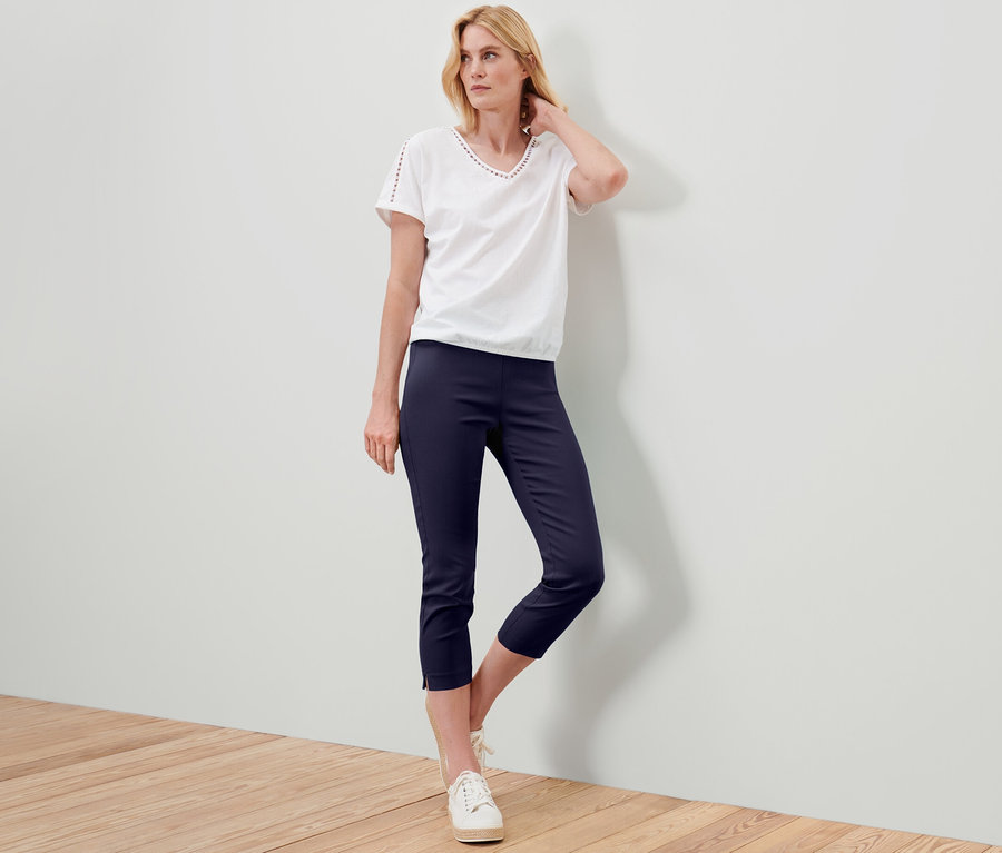 Frau posiert in weißem T-Shirt und dunkelblauer 7/8-Stretchhose.