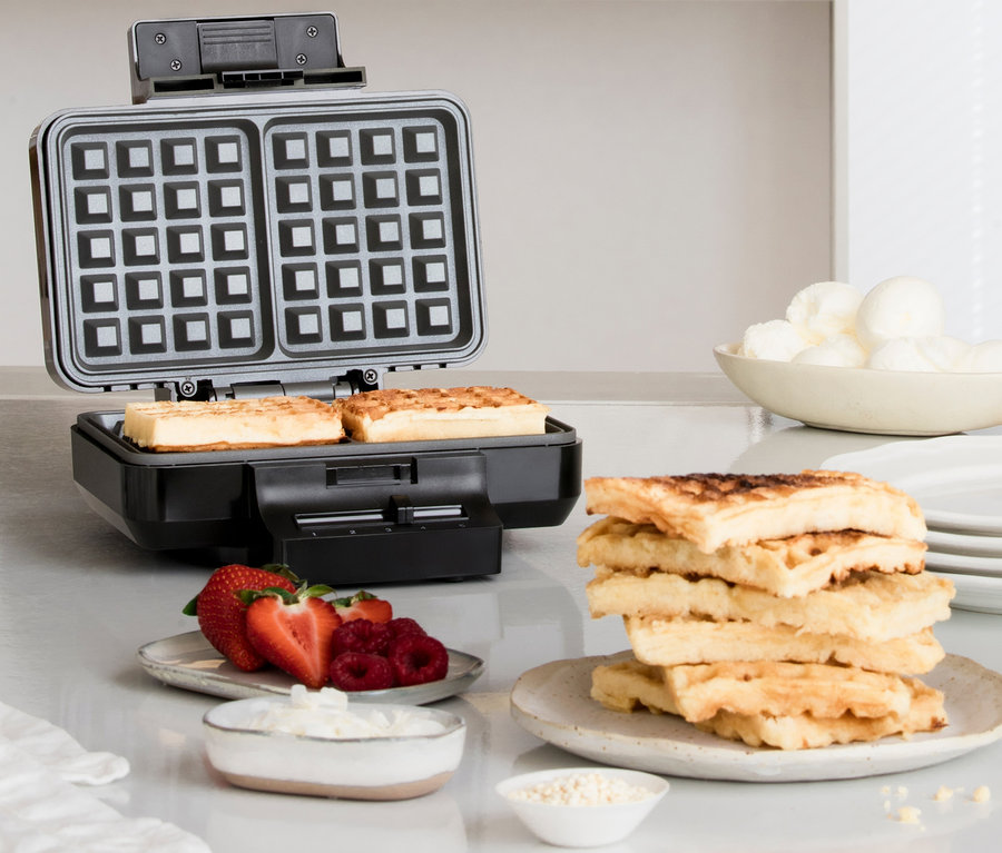 Auf einem Tisch stehen ein schwarzes WILFA Waffeleisen GAUFRES »BW-1000B«, Waffeln, Erdbeeren, Himbeeren, Schlagsahne und Eis.