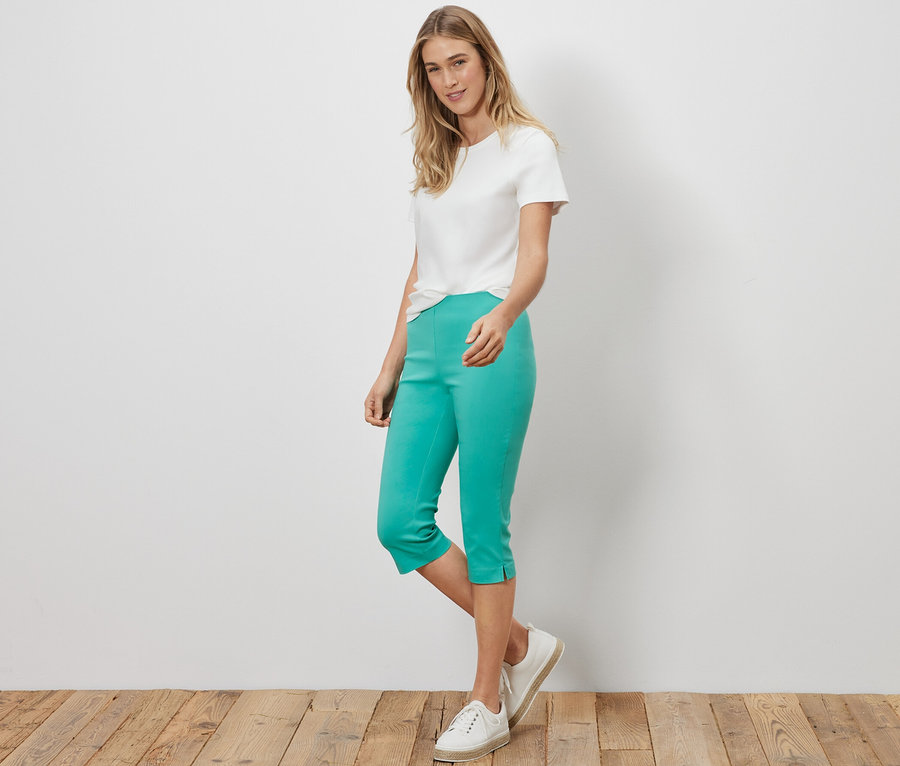 Frau steht und trägt ein weißes T-Shirt und eine türkise 3/4-Stretchhose.