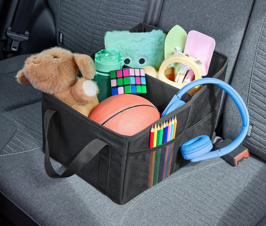 In einer schwarzen Tasche im Auto befinden sich Spielzeug, Buntstifte, Kopfhörer und andere Gegenstände.