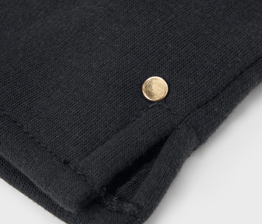 Detailaufnahme eines schwarzen Stoffes mit einem kleinen goldenen Knopf.