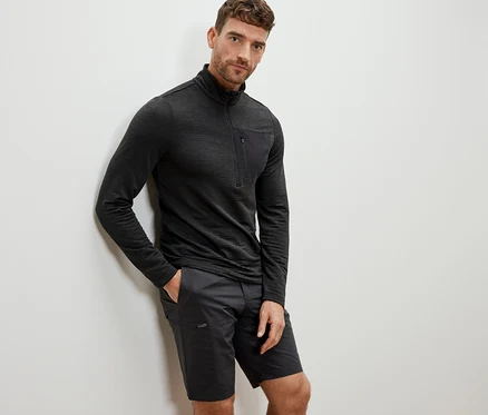 Mann lehnt an Wand, trägt anthrazitfarbenes Outdoor-Funktionsshirt und Shorts.