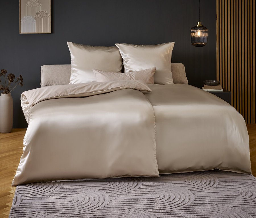 Schlafzimmer mit einem Bett mit beiger Satinbettwäsche und einem dekorativen Teppich.