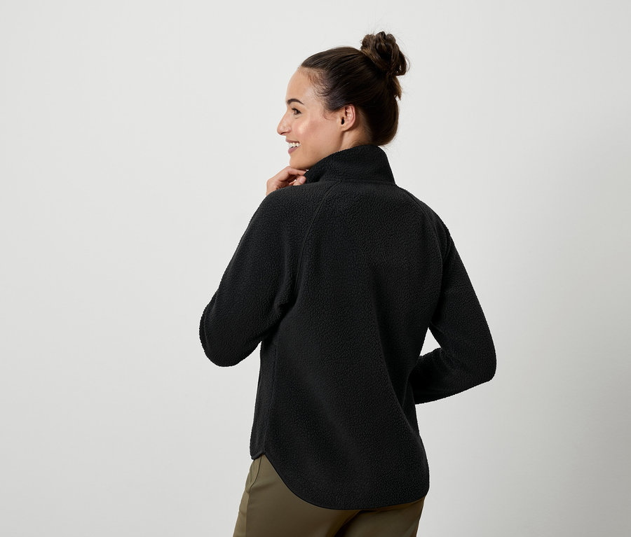 Frau blickt über die Schulter und trägt ein schwarzes Fleecepullover und Khakihosen.