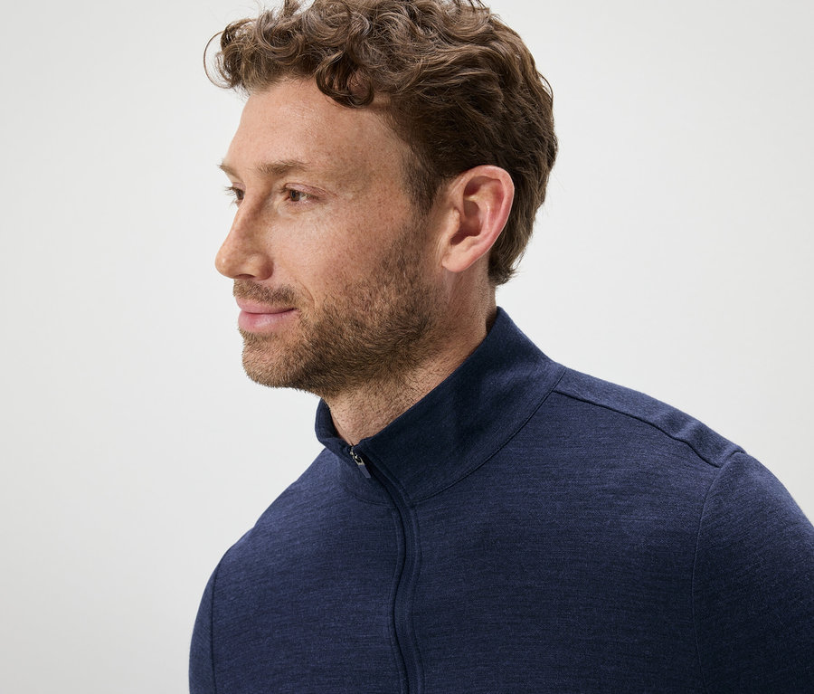 Porträt eines Mannes mit braunen, gewellten Haaren und Bart, der einen blauen Reißverschluss-Pullover trägt.