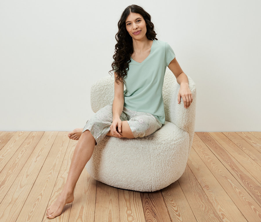 Eine Frau sitzt in einem Sessel und trägt ein hellgrünes 3/4-Pyjama-Set.