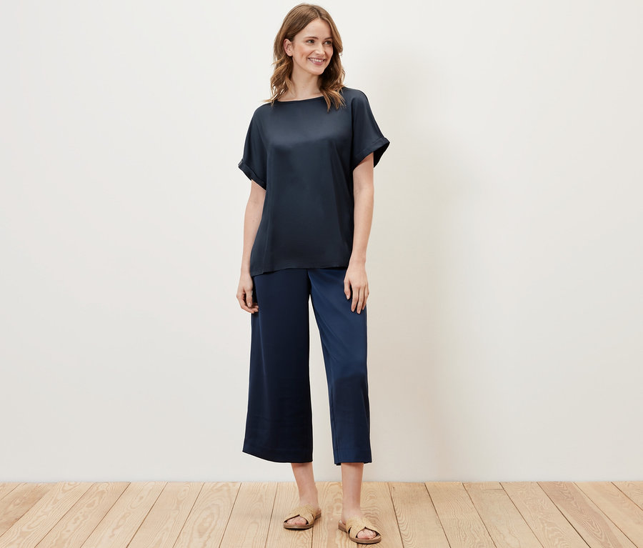 Frau trägt ein marineblaues Blusenshirt im Materialmix und blaue Hosen.