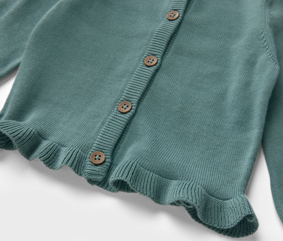 Detailansicht einer Kinder-Strickjacke mit Knöpfen und Rüschen.