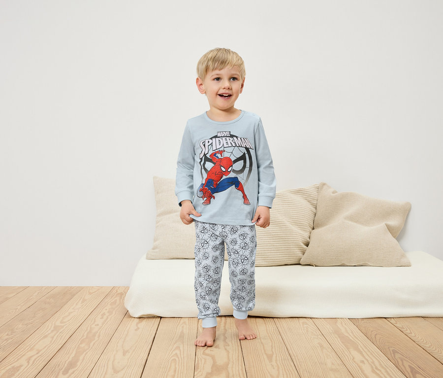 Ein Junge im Spiderman-Pyjama steht auf einem Holzboden vor einem weißen Sofa.