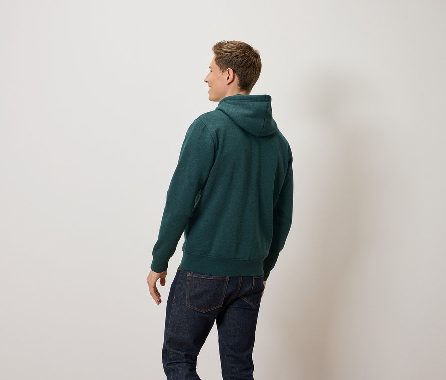 Mann schaut nach links und trägt einen grünen Kapuzenpullover und Jeans.