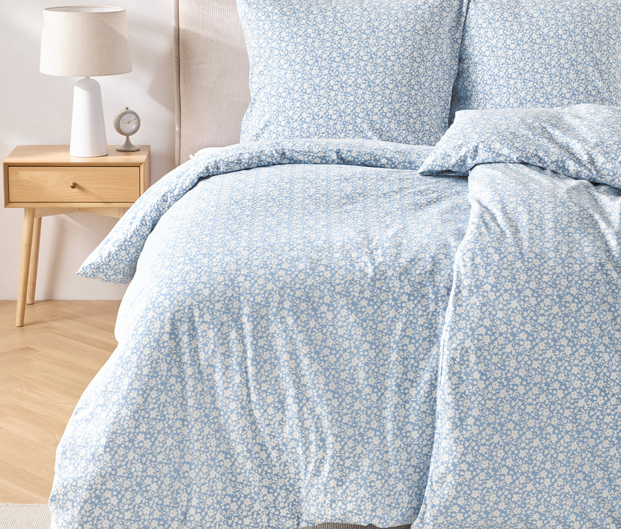 Nahaufnahme eines Bettes mit normalgroßer Jersey-Bettwäsche mit blau-weißem Blumenmuster.