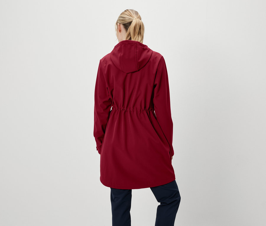 Eine Frau mit dem Rücken zur Kamera trägt eine rote Jacke mit Kapuze und dunkelblaue Hosen.