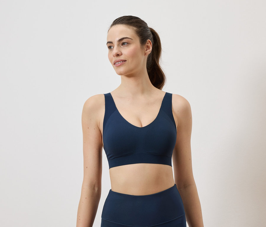 Frau mit Pferdeschwanz trägt marineblauen Sport-BH und Leggings vor einem weißen Hintergrund.