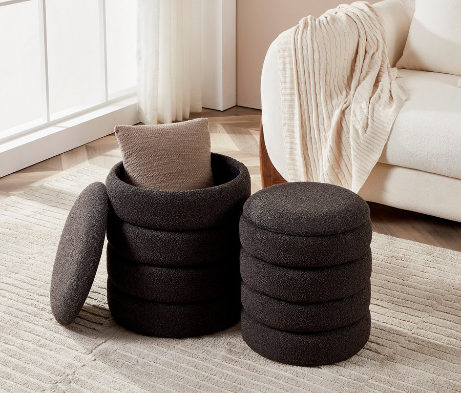 Ein grauer Hocker mit einem Kissen darin und ein weiterer grauer Hocker stehen auf einem Teppich.