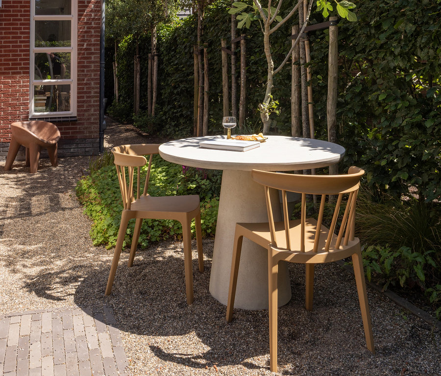 Zwei karamellfarbene WOOOD Gartenstühle stehen an einem runden Tisch im Garten.