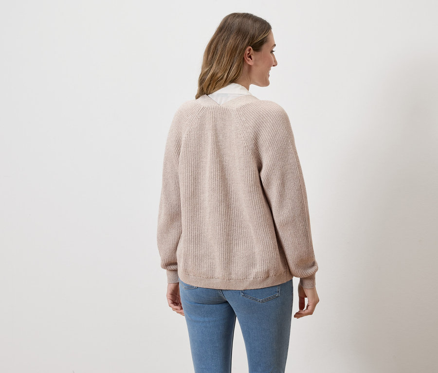 Frau von hinten in Jeans und beiger Strickjacke vor weißem Hintergrund.