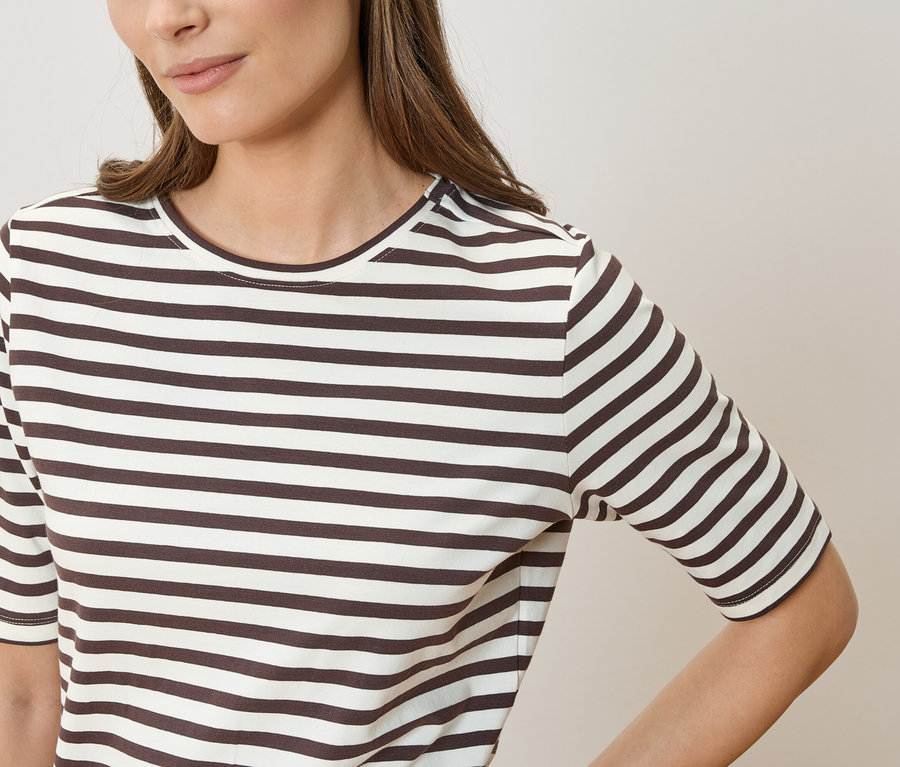 Frau mit braunen Haaren trägt ein gestreiftes T-Shirt in Braun und Weiß.