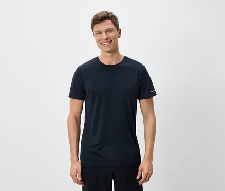 Ein Mann lächelt und trägt ein marineblaues T-Shirt und Shorts vor einem weißen Hintergrund.