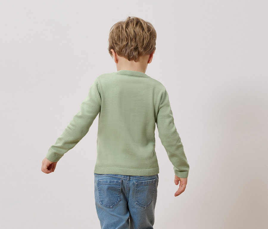 Rückansicht eines Kindes mit blonden Haaren, das einen hellgrünen Pullover und blaue Jeans trägt.