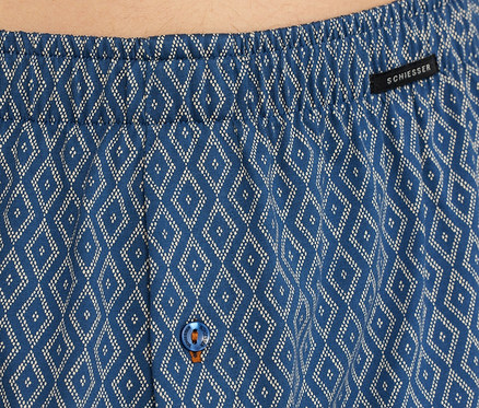 Nahaufnahme einer blauen SCHIESSER Jersey-Boxer mit weißem Rautenmuster, elastischem Bund, schwarzem SCHIESSER-Etikett und blauem Knopf mit orangefarbener Naht.