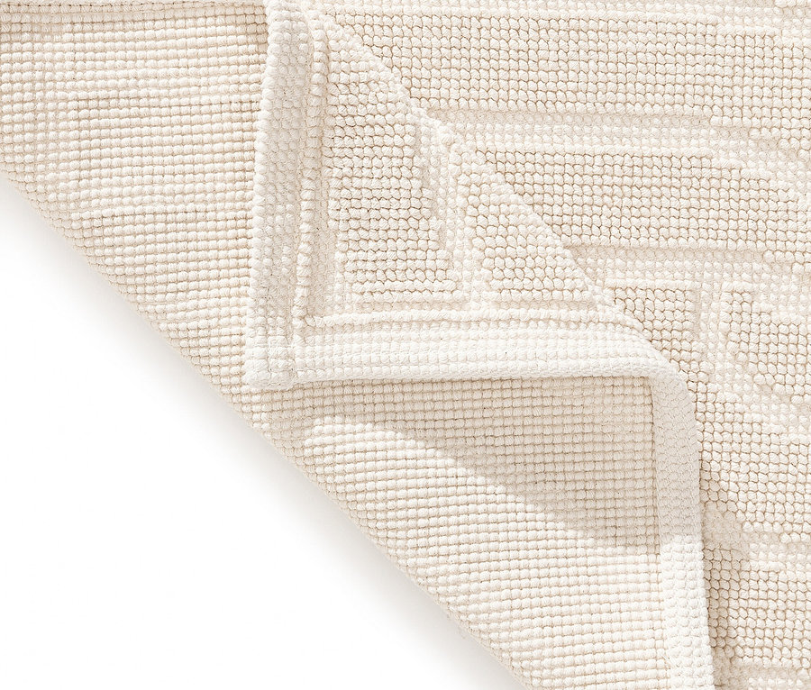 Nahaufnahme einer cremefarbenen Badematte mit geometrischem Muster, Ecke umgeschlagen.