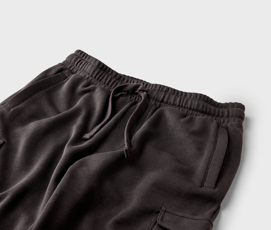 Nahaufnahme einer dunkelbraunen Jogginghose mit Kordelzug, elastischem Bund und Taschen auf grauem Hintergrund.