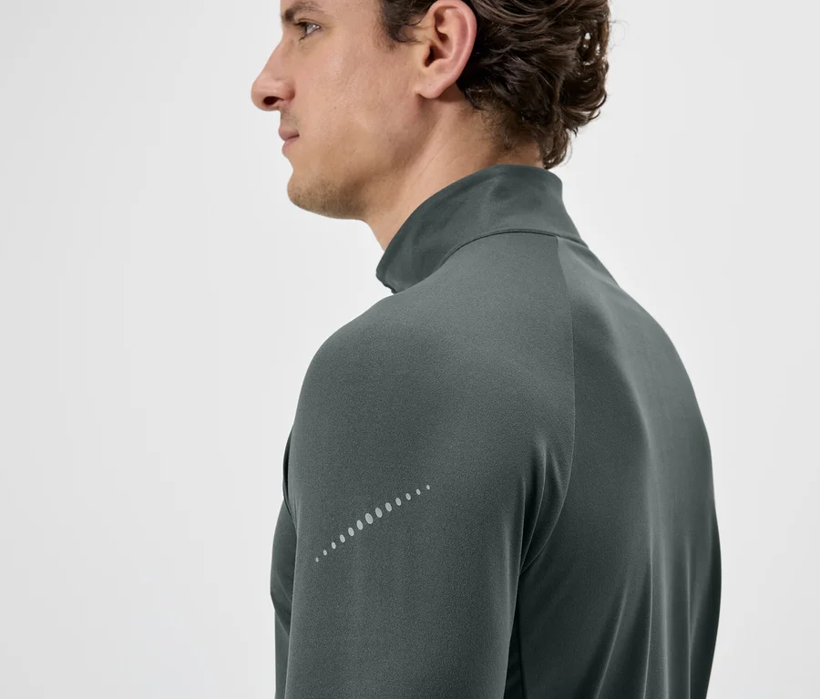 Nahaufnahme eines Mannes im Profil, der ein graues, langärmeliges Shirt mit Reißverschluss und reflektierenden Punkten am Ärmel trägt.