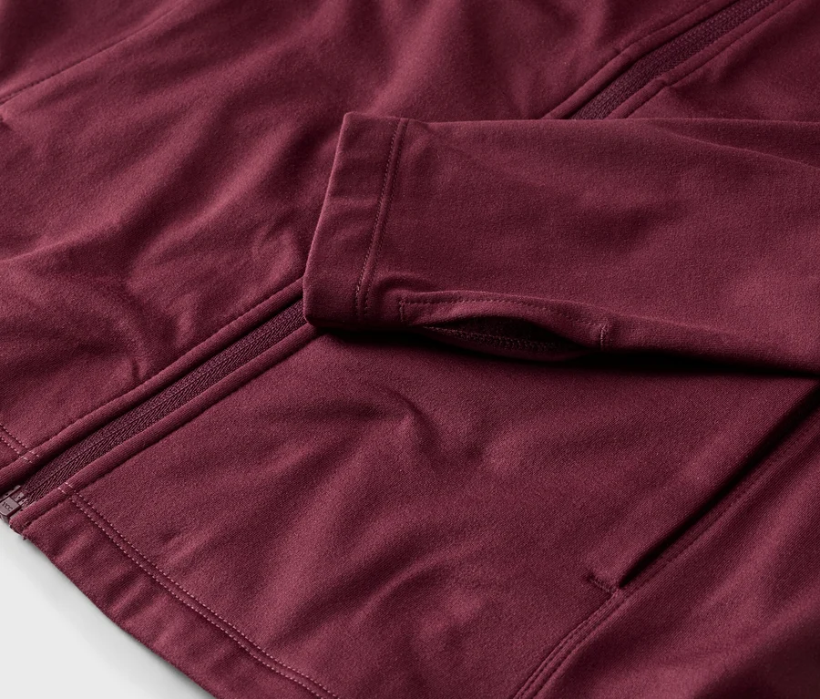 Nahaufnahme einer weinroten Jacke mit Reißverschluss und Daumenlöchern.