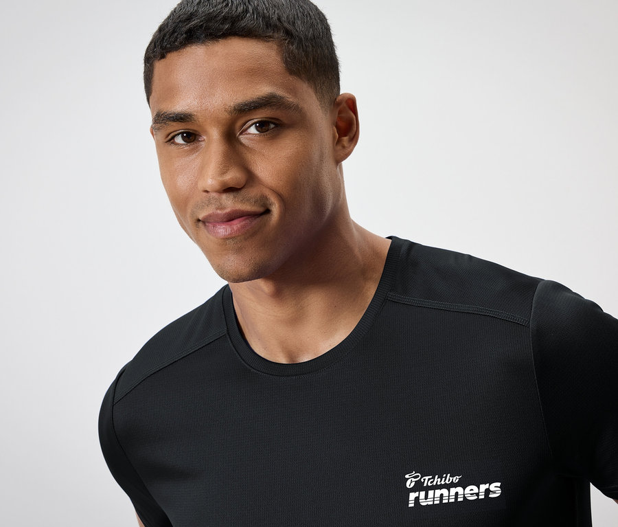 Ein Mann mit dunkler Haut trägt ein schwarzes T-Shirt mit dem Aufdruck "Tchibo runners".