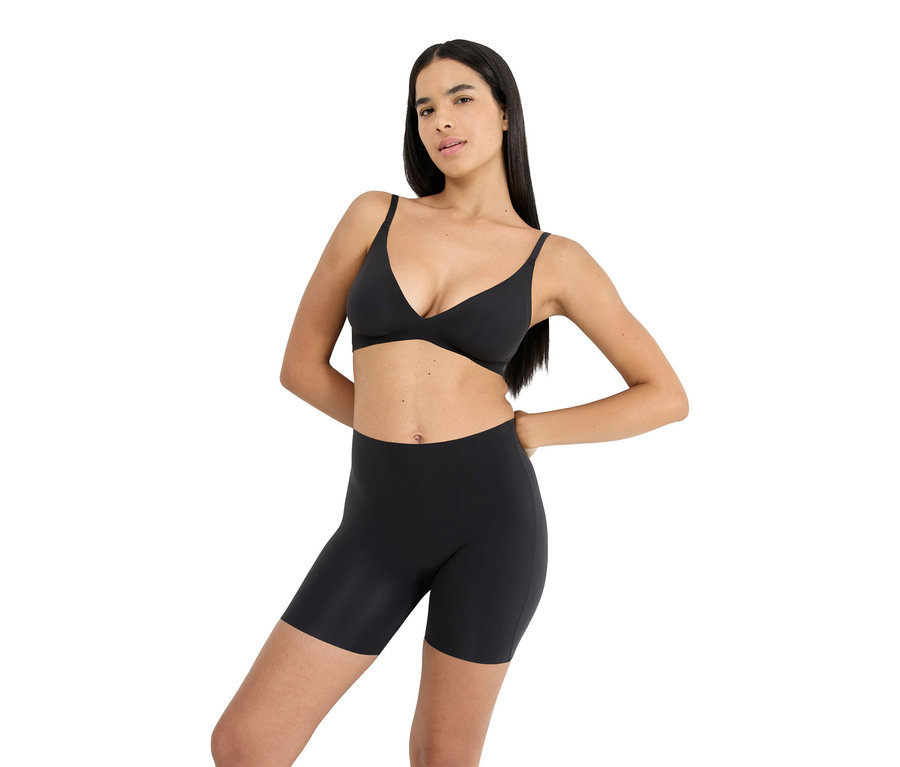 Frau mit langen dunklen Haaren, die einen schwarzen BH und schwarze Shorts trägt und ihre Hände auf ihre Hüften legt.