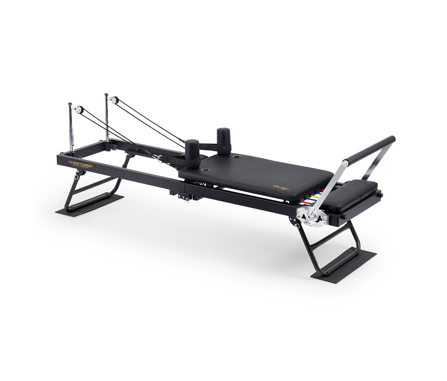 Schwarzer Pilates-Reformer mit gepolstertem Wagen, verstellbarer Fußstange, Schulterstützen und Seilen mit Rollen, darunter bunte Widerstandsfedern.
