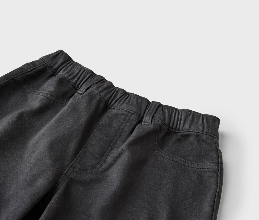 Nahaufnahme einer schwarzen Hose mit elastischem Bund, Gürtelschlaufen und Vordertaschen mit sichtbaren Nähten.