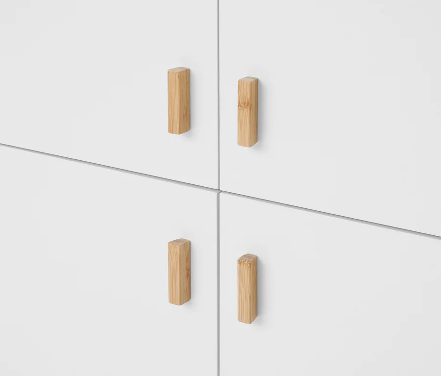 Vier weiße Schranktüren oder Schubladenfronten, jede mit einem vertikalen, rechteckigen Griff aus hellem Holz.