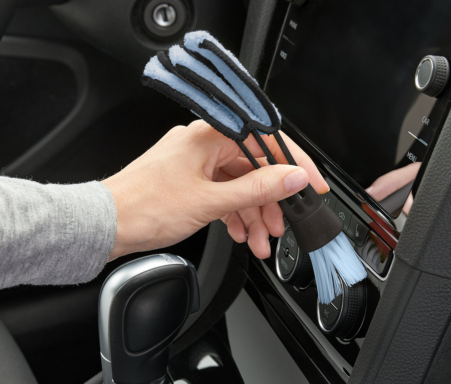 Eine Hand benutzt eine 2-in-1-Reinigungsbürste, um das Armaturenbrett eines Autos zu reinigen.