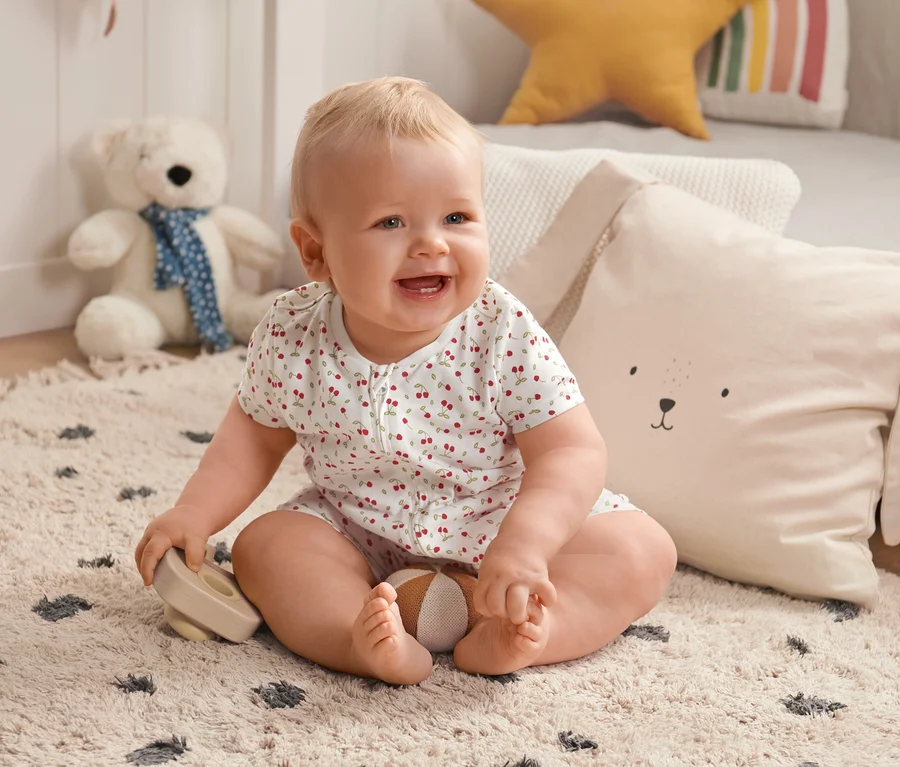 Lächelndes Baby sitzt auf einem Teppich und trägt einen 2 Shorty-Pyjama.