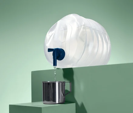 Wasser läuft aus einem faltbaren Wasserkanister in einen Metallbecher.