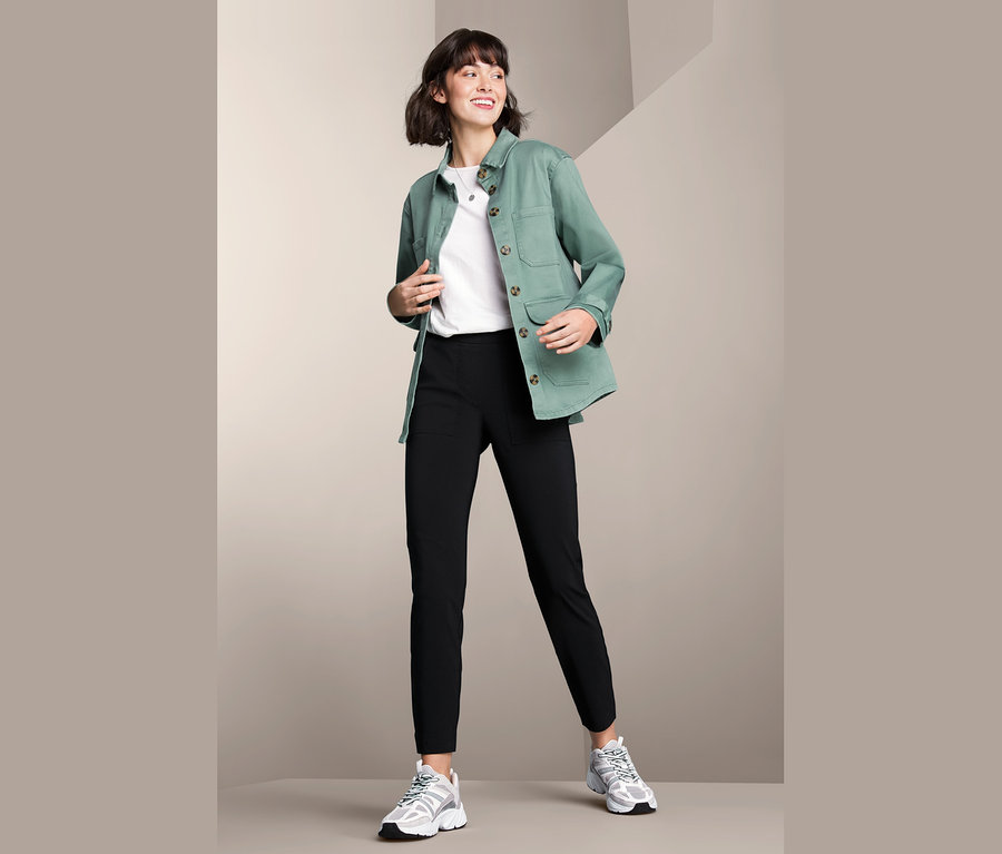 Frau posiert in Cargojacke, weißem T-Shirt und schwarzer Hose.