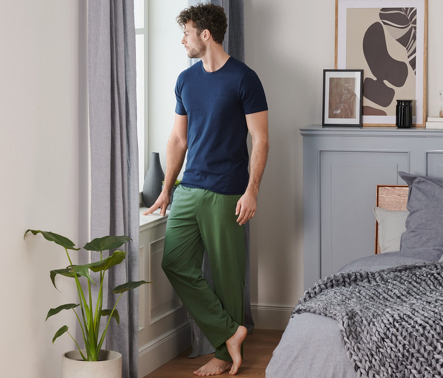 Mann im Pyjama lehnt am Fensterbrett und schaut aus dem Fenster.