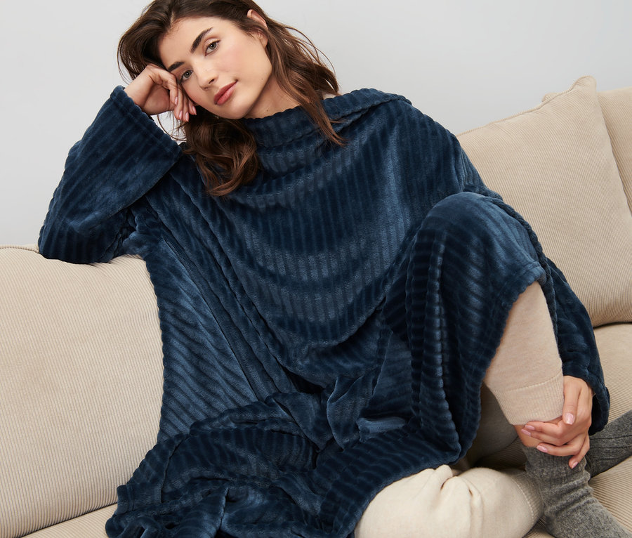 Frau sitzt auf einem Sofa und trägt eine Kuscheldecke mit integrierten Ärmeln.