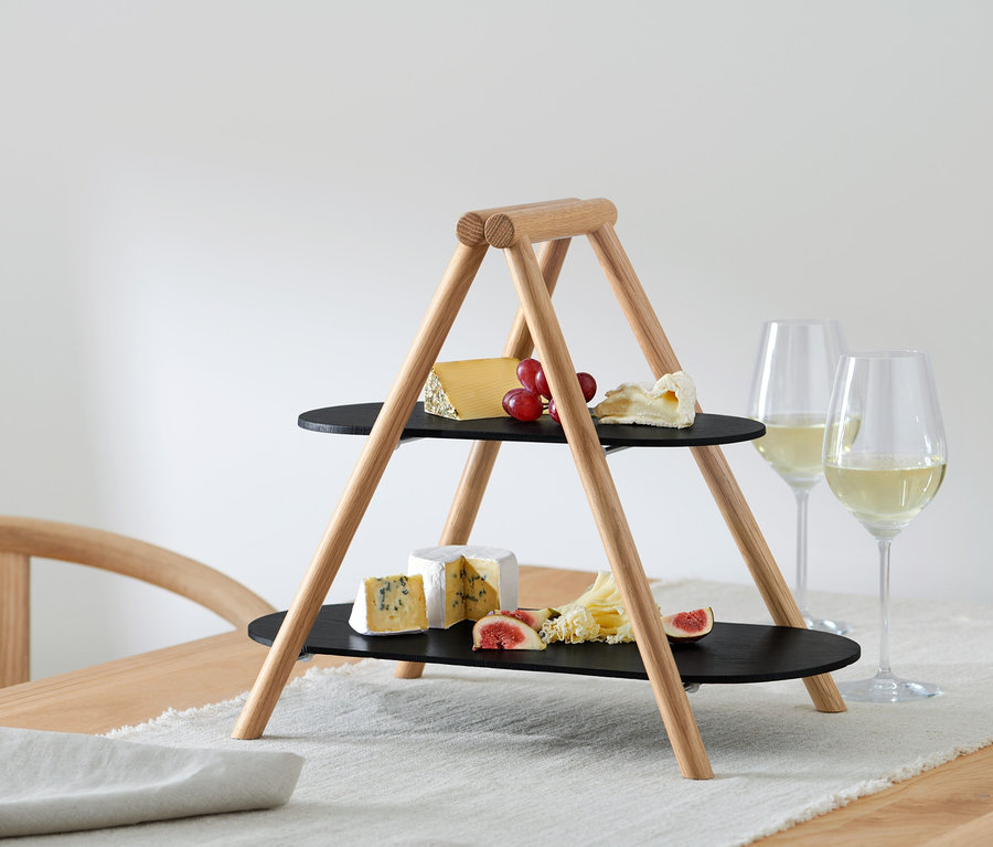 Zweistöckige Etagere mit Käse, Trauben und Feigen steht neben Weingläsern auf einem Tisch.