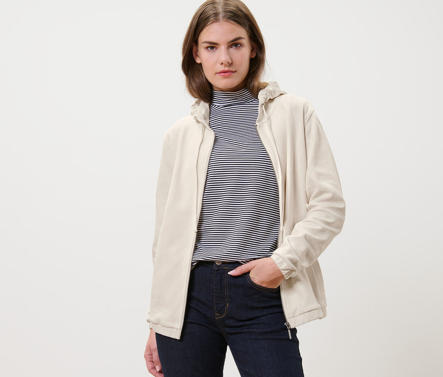 Frau trägt eine cremeweiße Sweatjacke und Jeans.