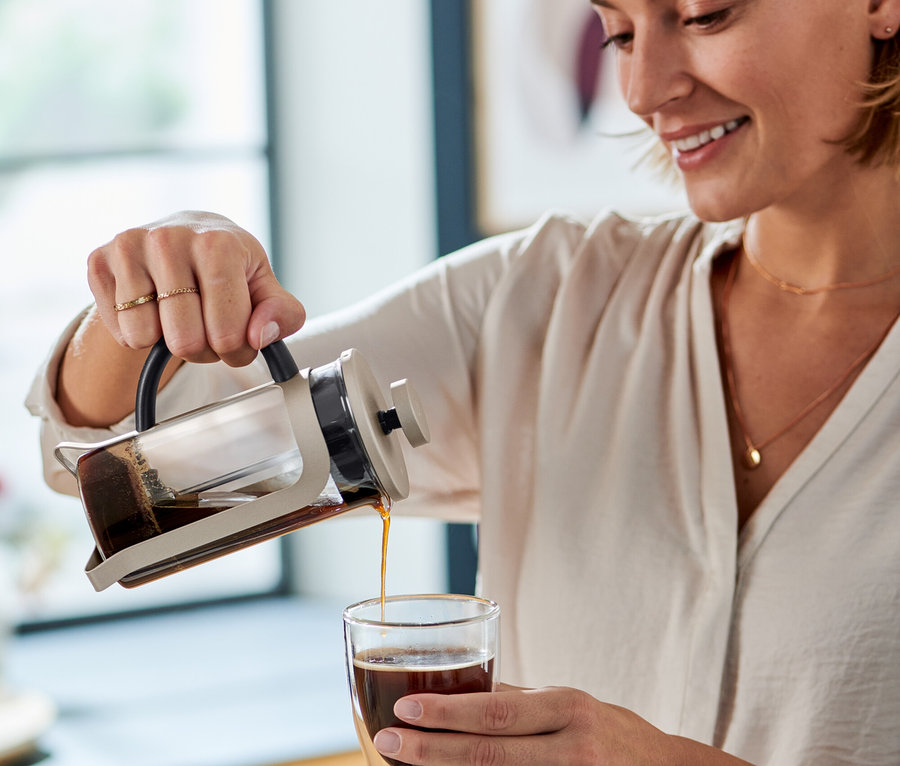Frau gießt Kaffee aus einer Siebstempelkanne 300 ml Champagner in ein Glas.