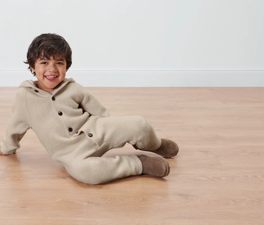 Ein Junge liegt auf dem Boden und trägt einen Baby-Merino-Walkoverall.