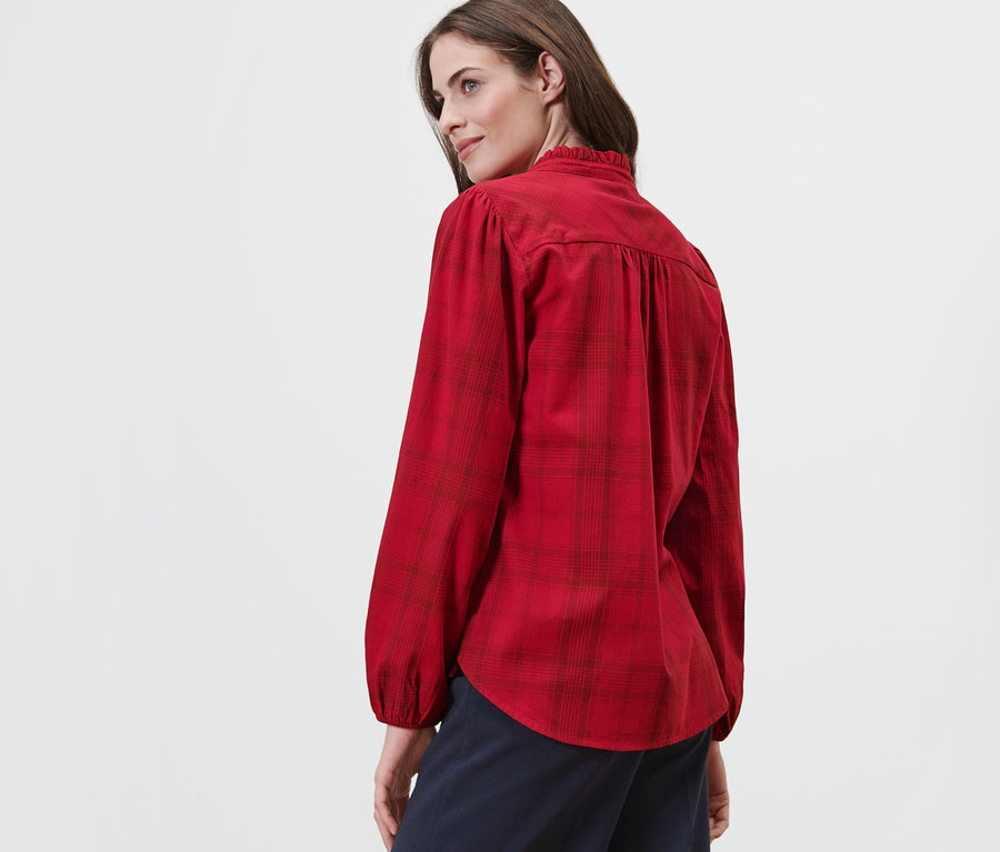 Frau blickt über ihre Schulter und trägt eine karierte Schluppenbluse.