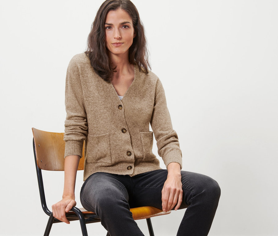 Frau sitzt auf Stuhl und trägt Strickjacke mit Wolle.