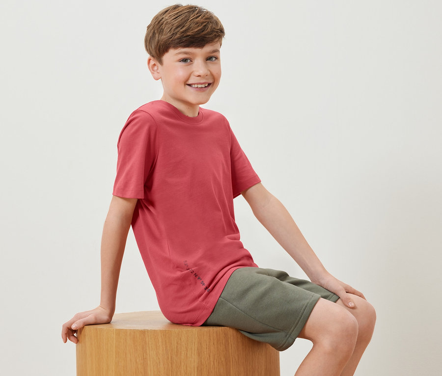 Ein Junge sitzt auf einem Holzwürfel und trägt ein rotes T-Shirt aus dem 2 Kinder-T-Shirts Set.