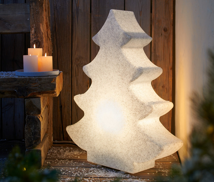 Eine Smart-LED-Outdoorleuchte »Tanne« steht auf einem Holzboden neben einer Holzbank mit brennenden Kerzen.