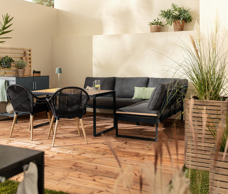 Eine Dining-Lounge-Ecke »Elin« mit Premium-Komfort-Kissen, dazu 2 Pflanzsäulen »Tinus«, eine LED-Akku-Tischleuchte in Salbei und ein Schalenstuhl mit Textilgeflecht.