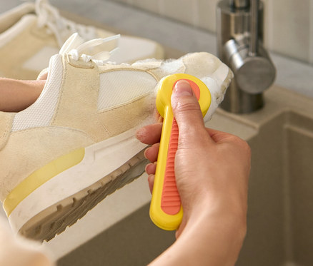 Frau putzt einen Schuh mit einer Schuhbürste über einem Waschbecken.