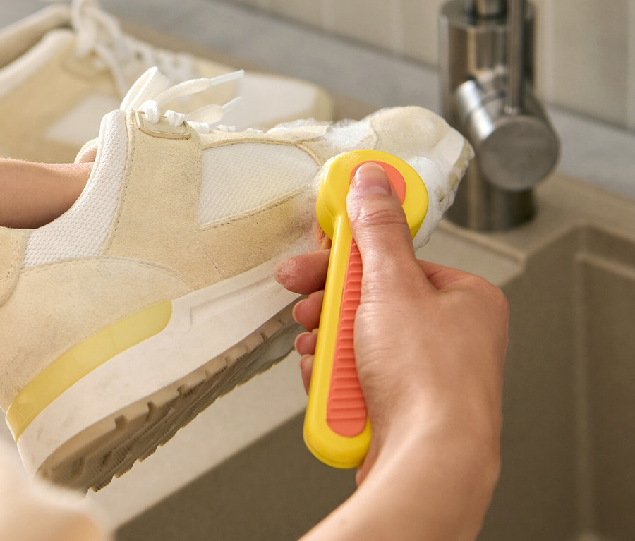 Frau putzt einen Schuh mit einer Schuhbürste über einem Waschbecken.